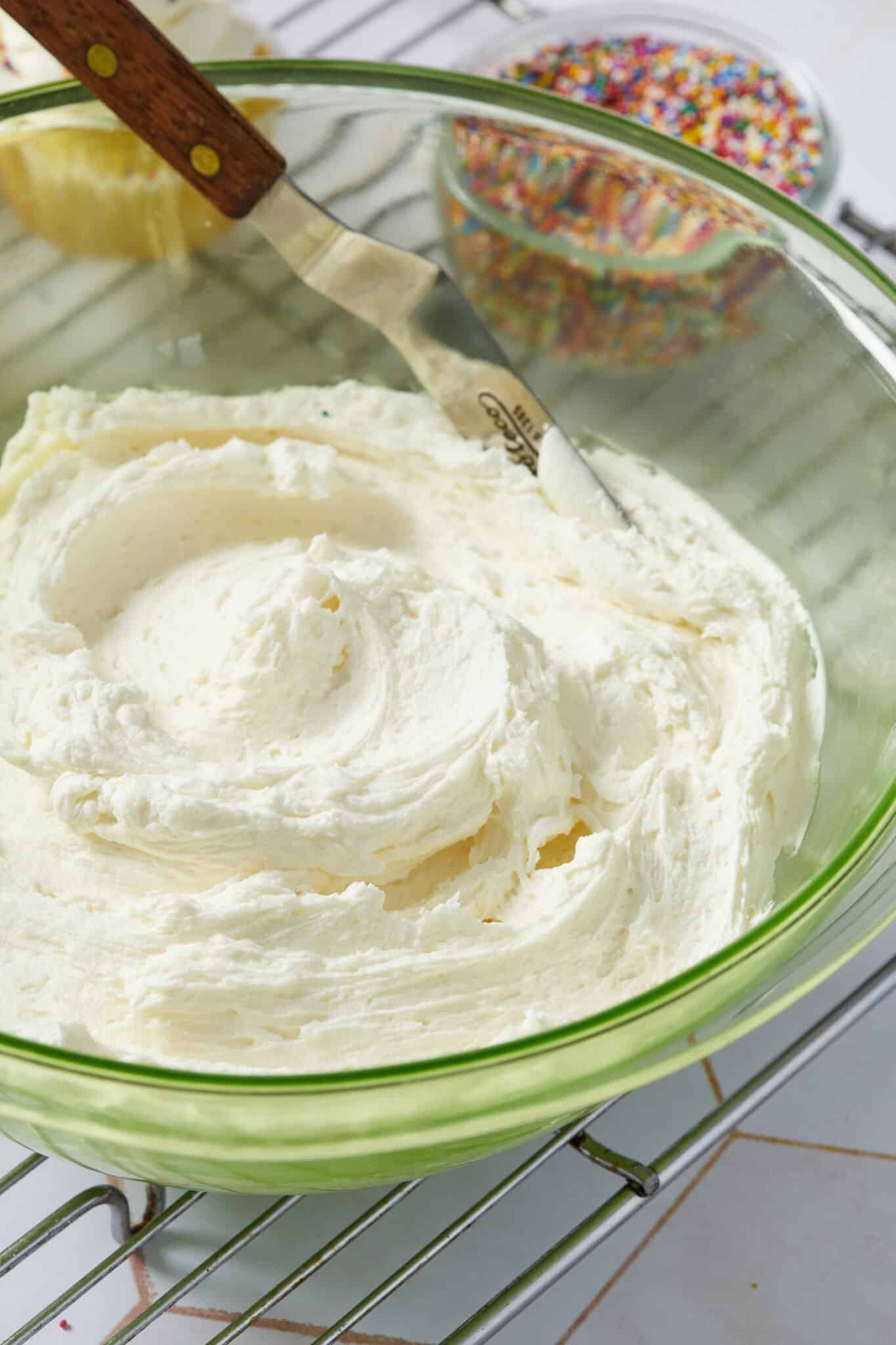 Smooth and creamy Best-Ever Buttercream Frosting in a big glass bowl, ready to use with sprinkles. 