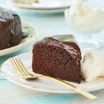 A slice of chocolate Guinness cake on a plate with fresh cream next to a gold fork.