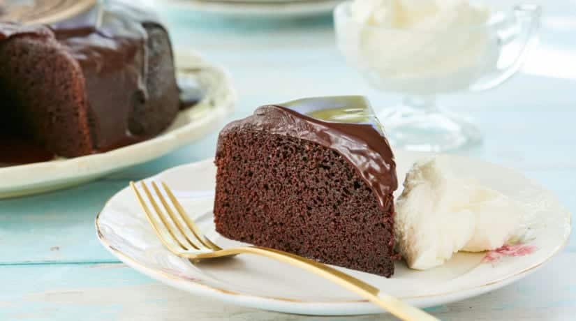 A slice of chocolate Guinness cake on a plate with fresh cream next to a gold fork.