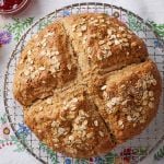 A big loaf of rustic, golden Irish soda bread with a cross scoring and topped with rolled oats.
