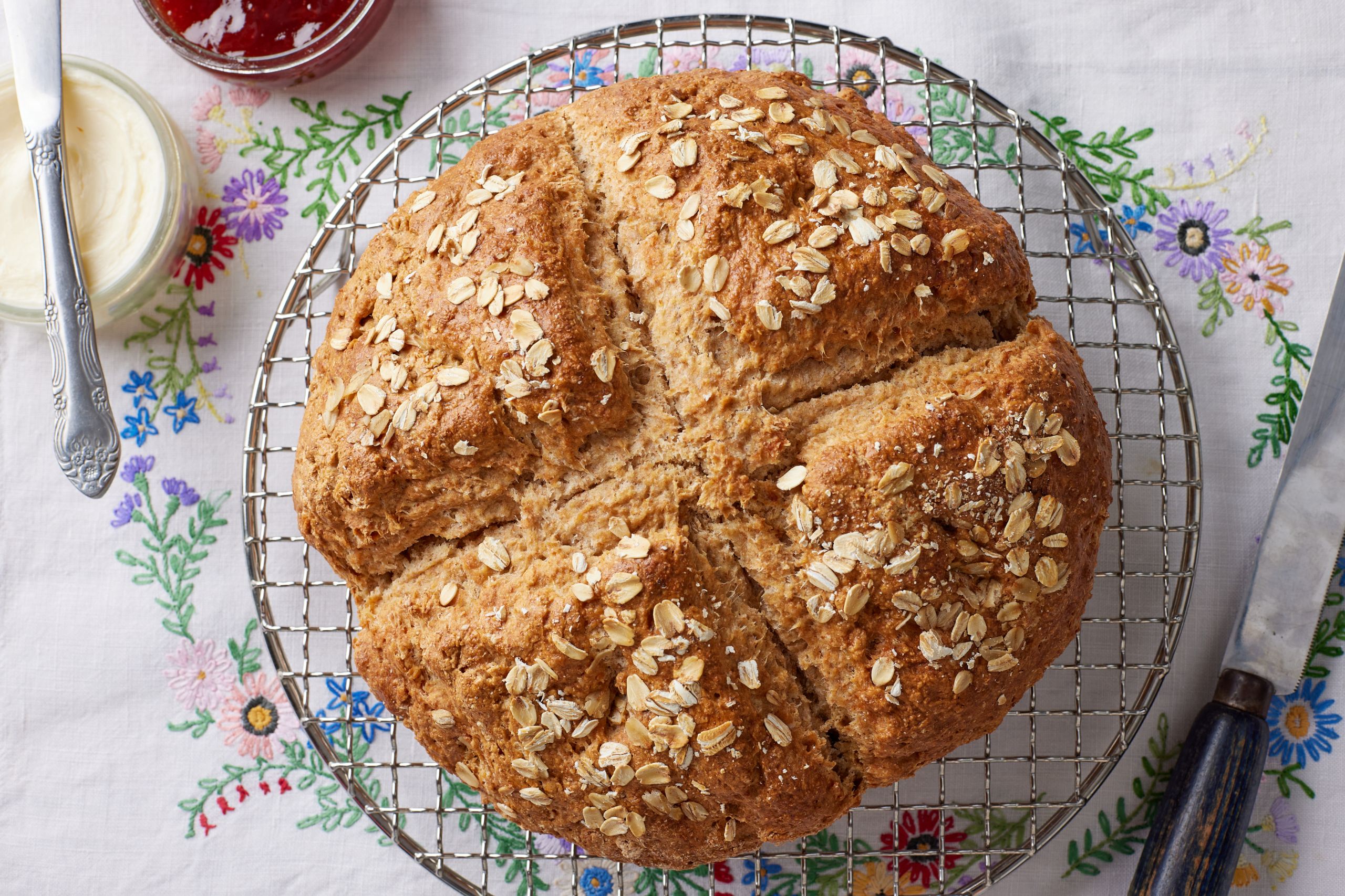 A big loaf of rustic, golden Irish soda bread with a cross scoring and topped with rolled oats.