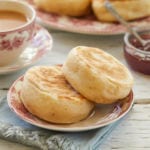 Two sourdough English muffins on a dish next to a cup of tea.