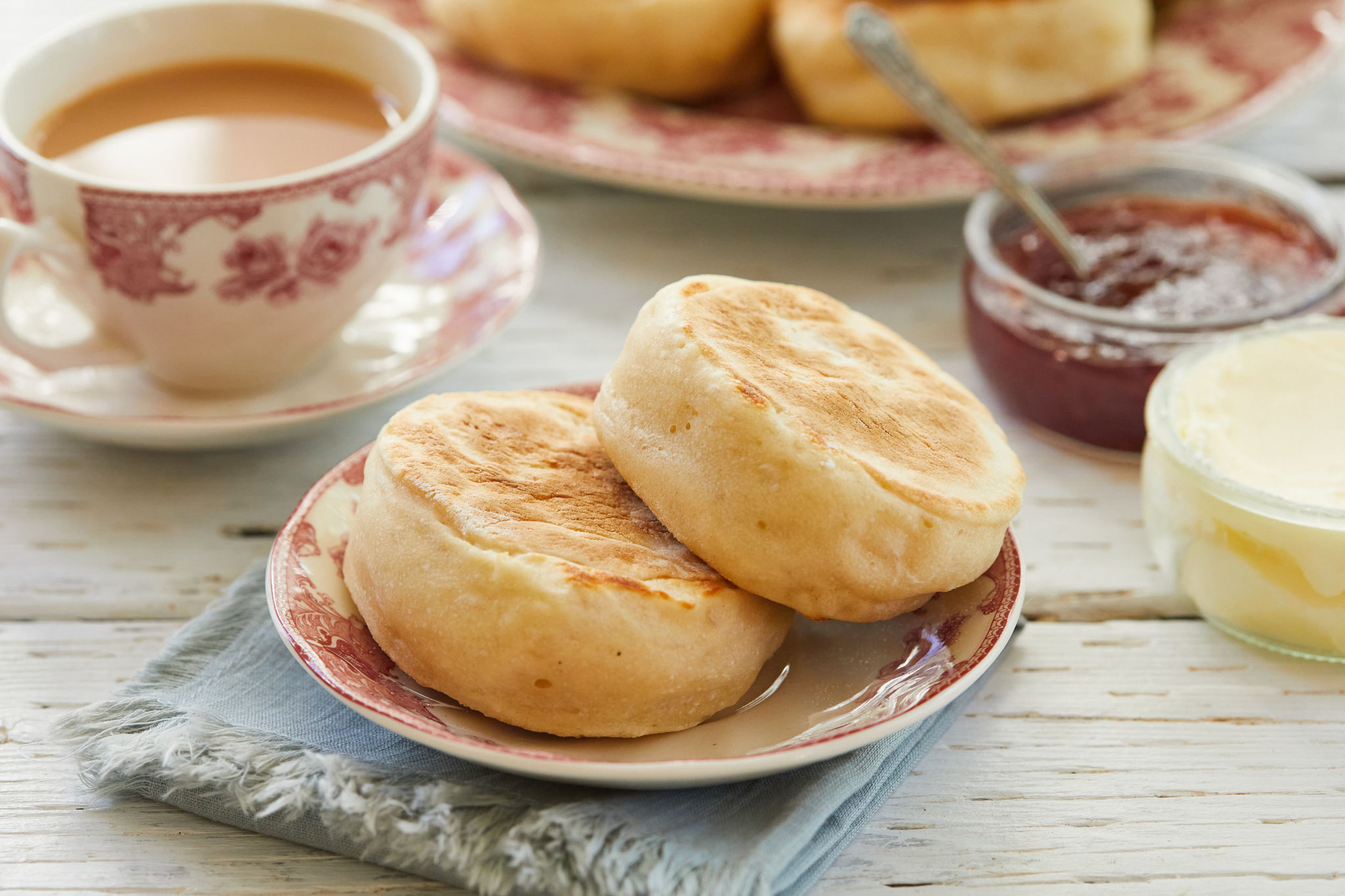 Two sourdough English muffins on a dish next to a cup of tea.