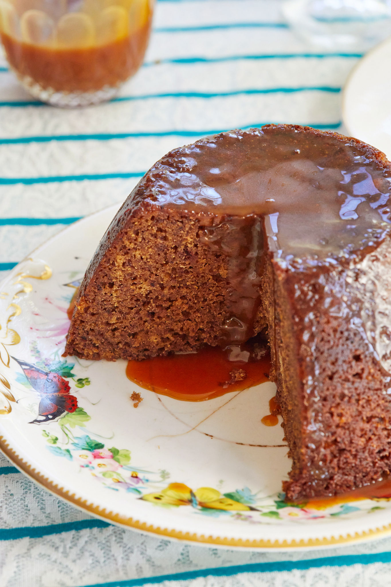 Sticky Toffee Pudding recipe dripping onto a plate, with a slice taken out to show texture and consistency.