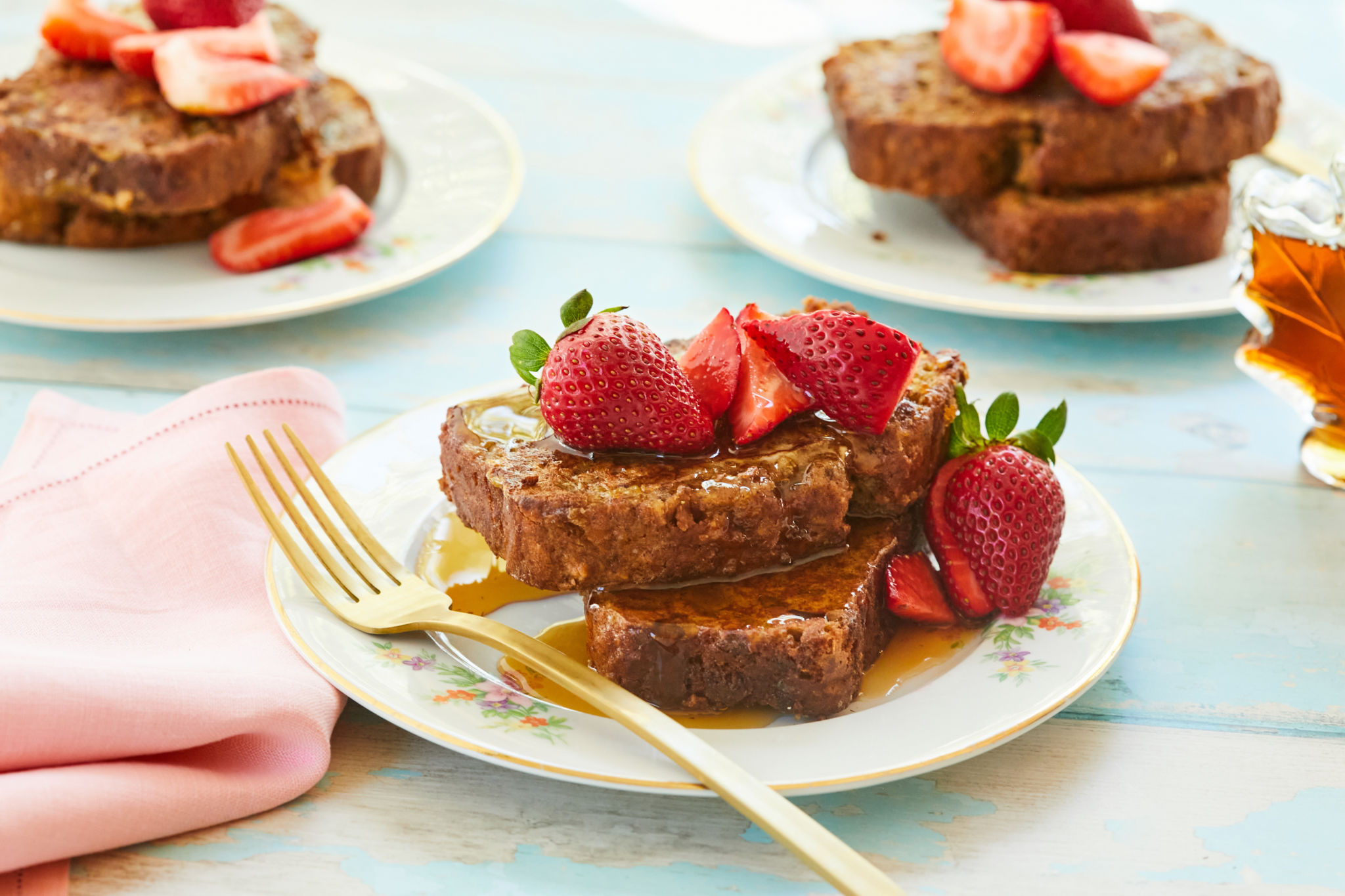Plates of Banana Bread French Toast topped with syrup and strawberries.
