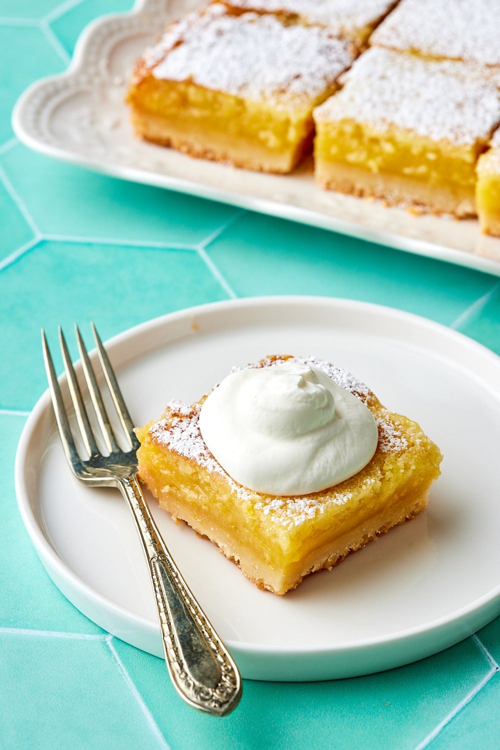 Easy Lemon Bars9 One piece of Lemon bar is served with softly whipped cream, with the rest of the lemon bars in the back.