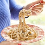 A bowl of homemade pici pasta being spun on a fork.