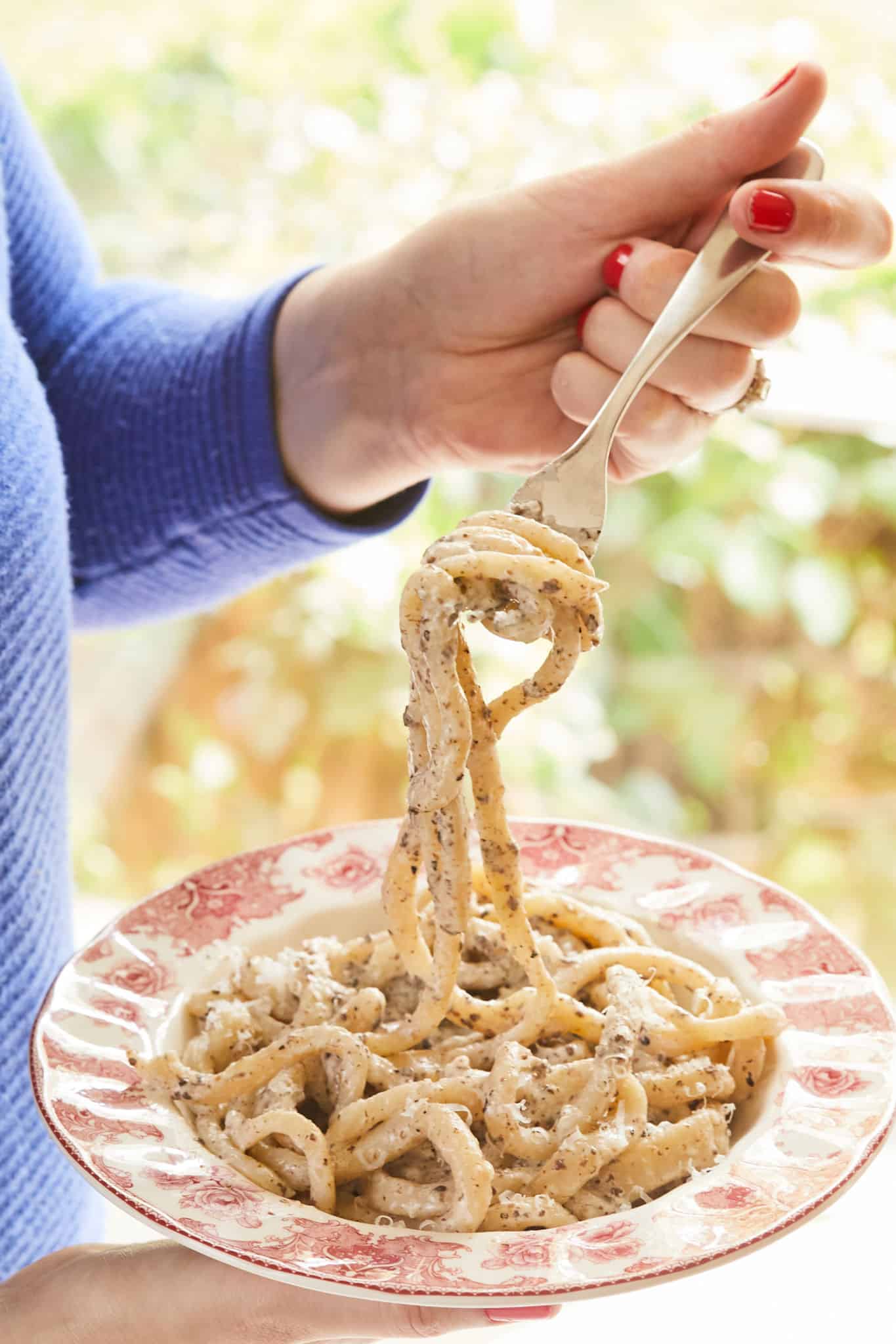 A hand holding a forkful of pici pasta with sauce.