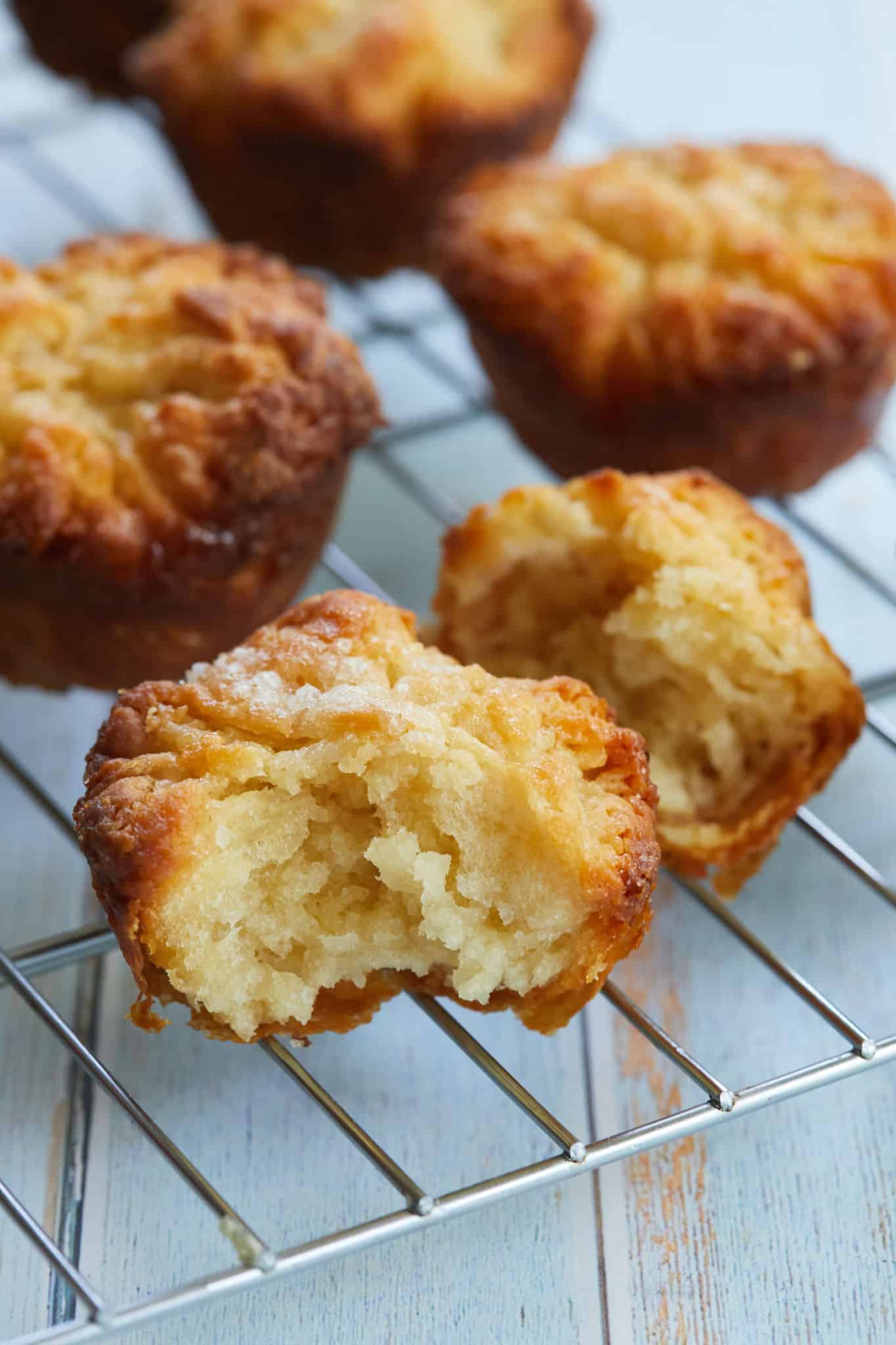 A close up of Kouign-Amann pastries on the cooling rack. They're golden brown with flakey layers. One has one bite taken, showing the soft inside.
