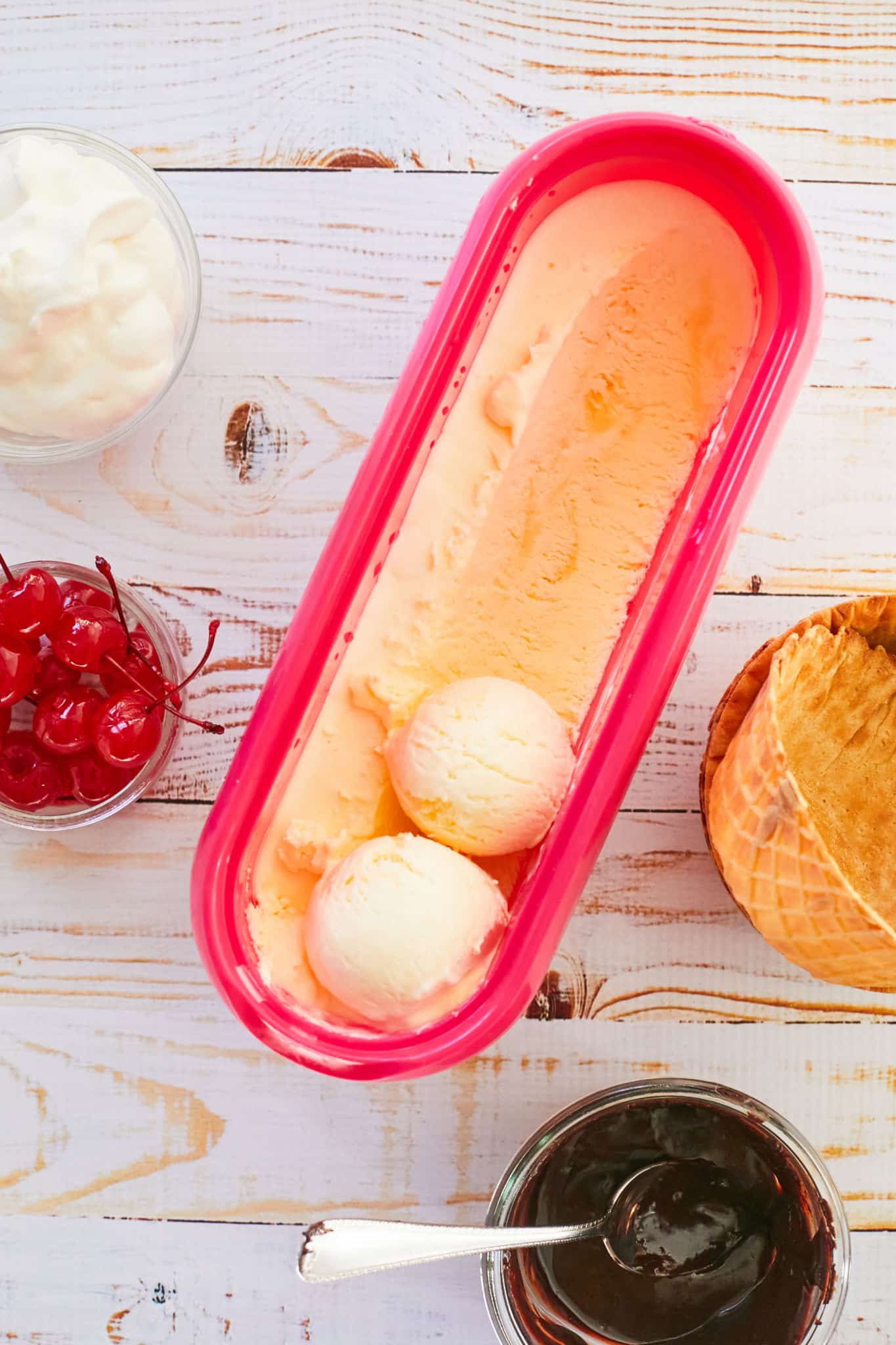 A tub with scoops of vanilla pudding ice cream in it, next to toppings.