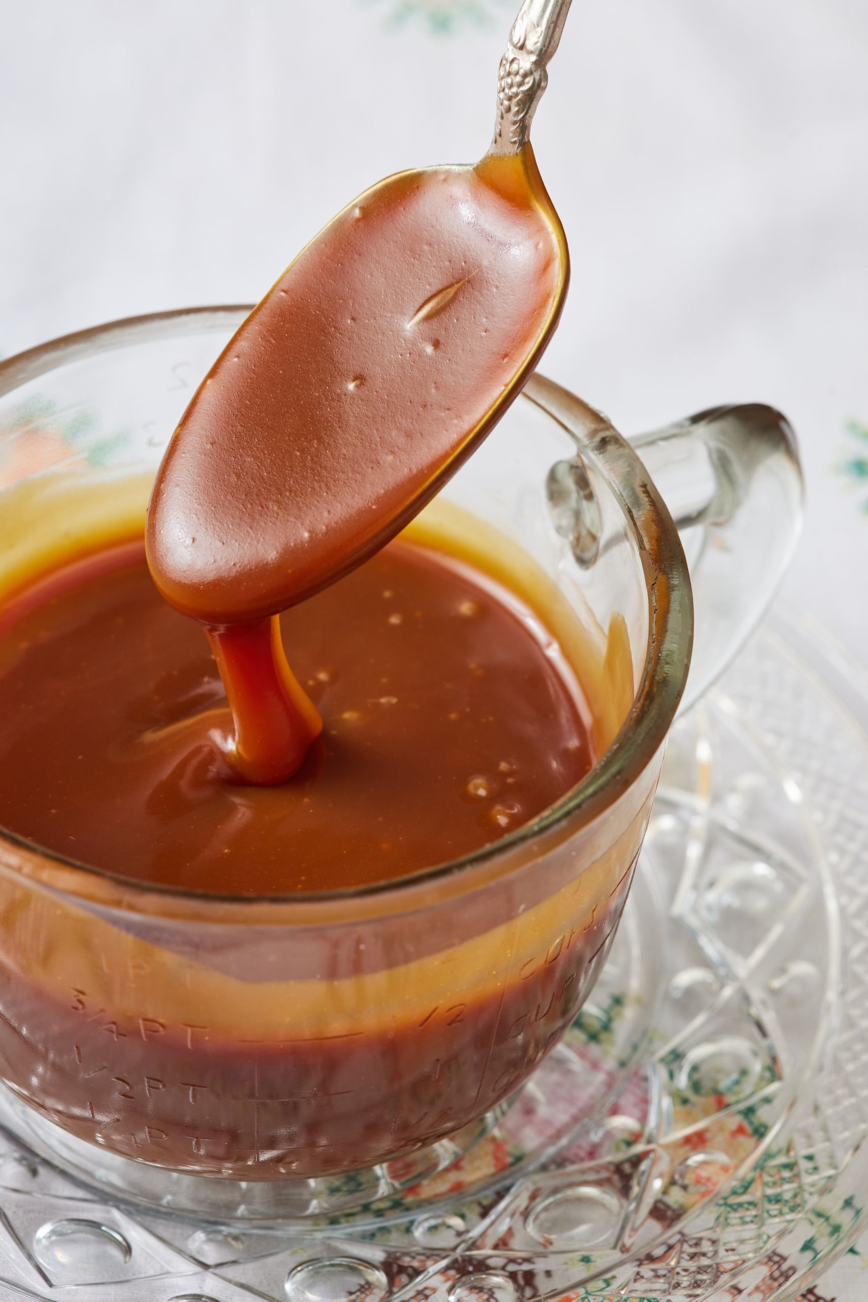 A jug of smooth salted caramel with a spoonful dipping back into the jug. 