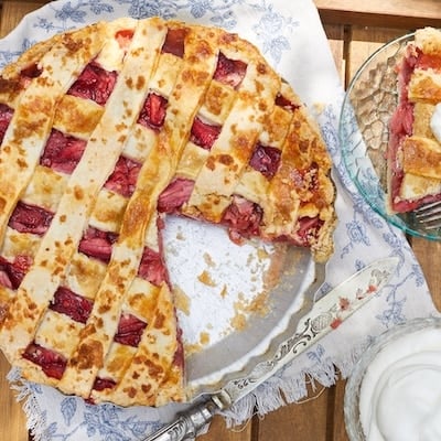A strawberry pie with a piece cut served on the side with whipped cream.