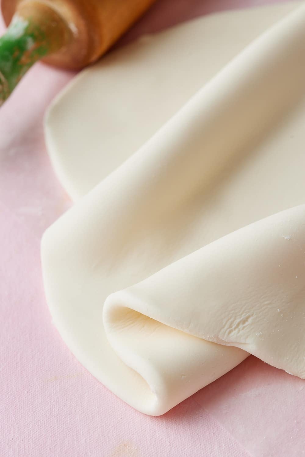 Fondant9 Close-up of smooth, white homemade fondant rolled into a soft sheet on a pink surface.