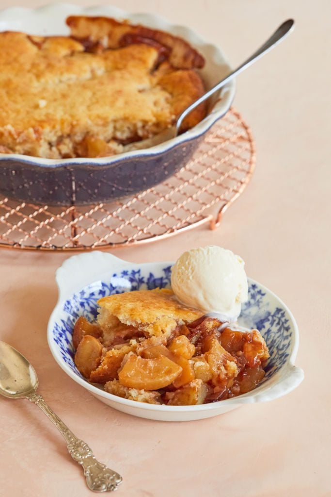 Apple Honey Cobbler is served with a scoop of ice cream, with the baking dish of remaining cobbler in the back.