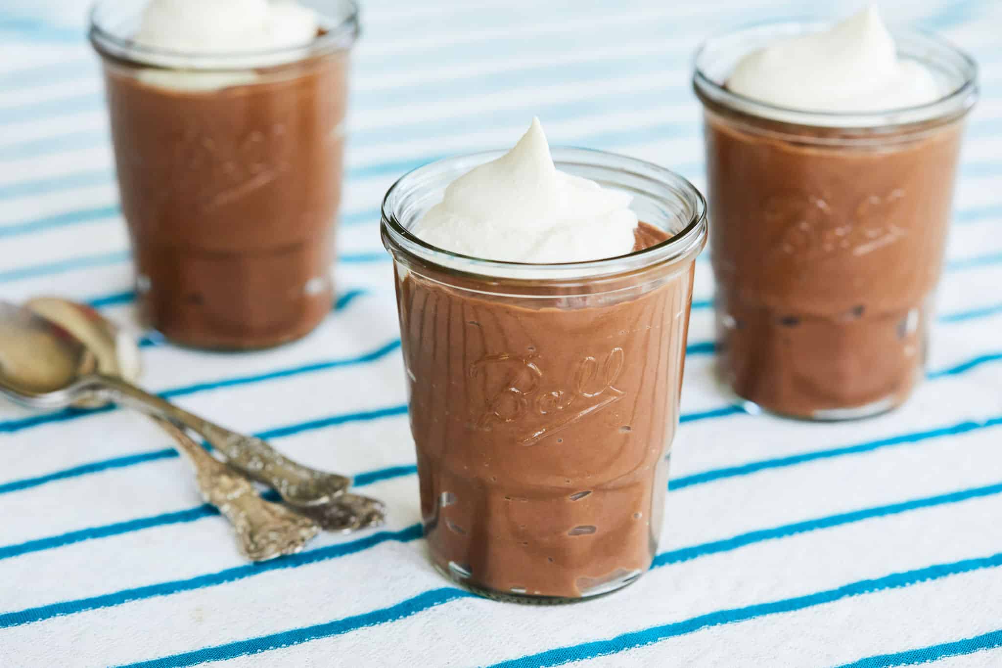 Three jars of chocolate pudding with whipped cream on top.