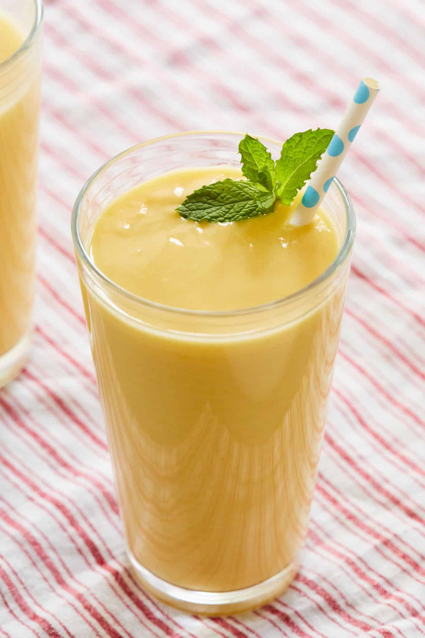 A glass of my Mango Lassi recipe topped with mint and a straw.