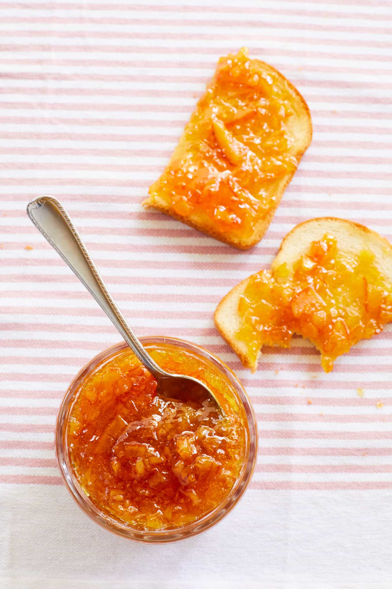 A jar of orange marmalade next to some toast.