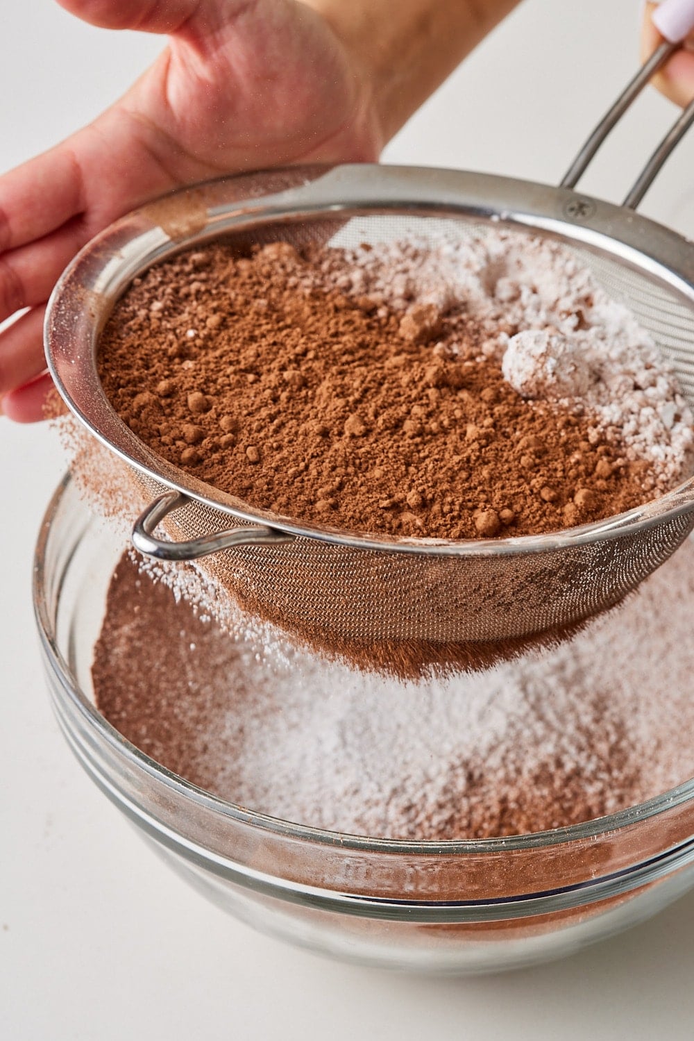 Sifting cocoa powder and sugar into a glass bowl for Chocolate Buttercream Recipe. 