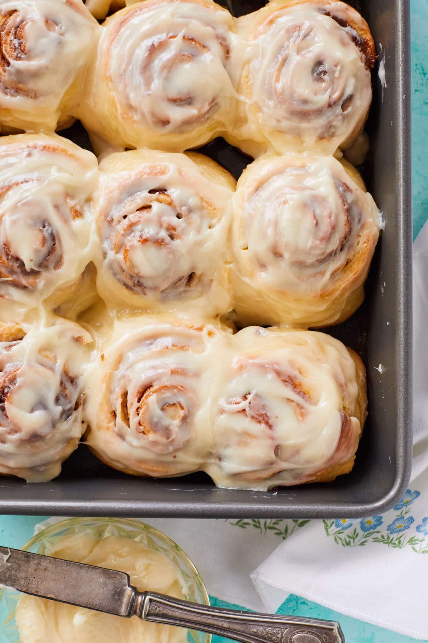A top-down view of homemade Cinnabon cinnamon rolls slathered in cream cheese frosting.