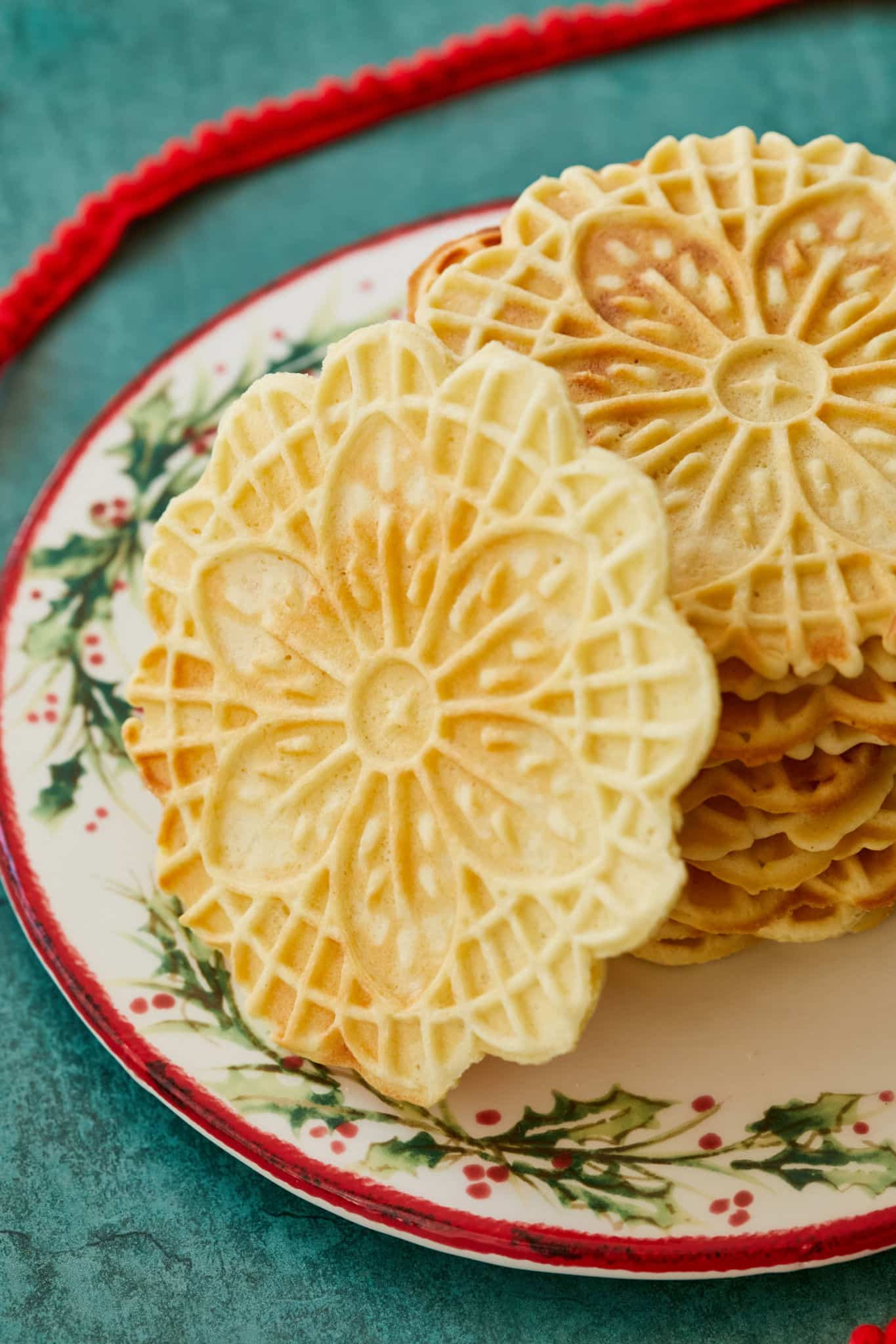A pizzelle leaning up against a stack of them on a holiday plate.