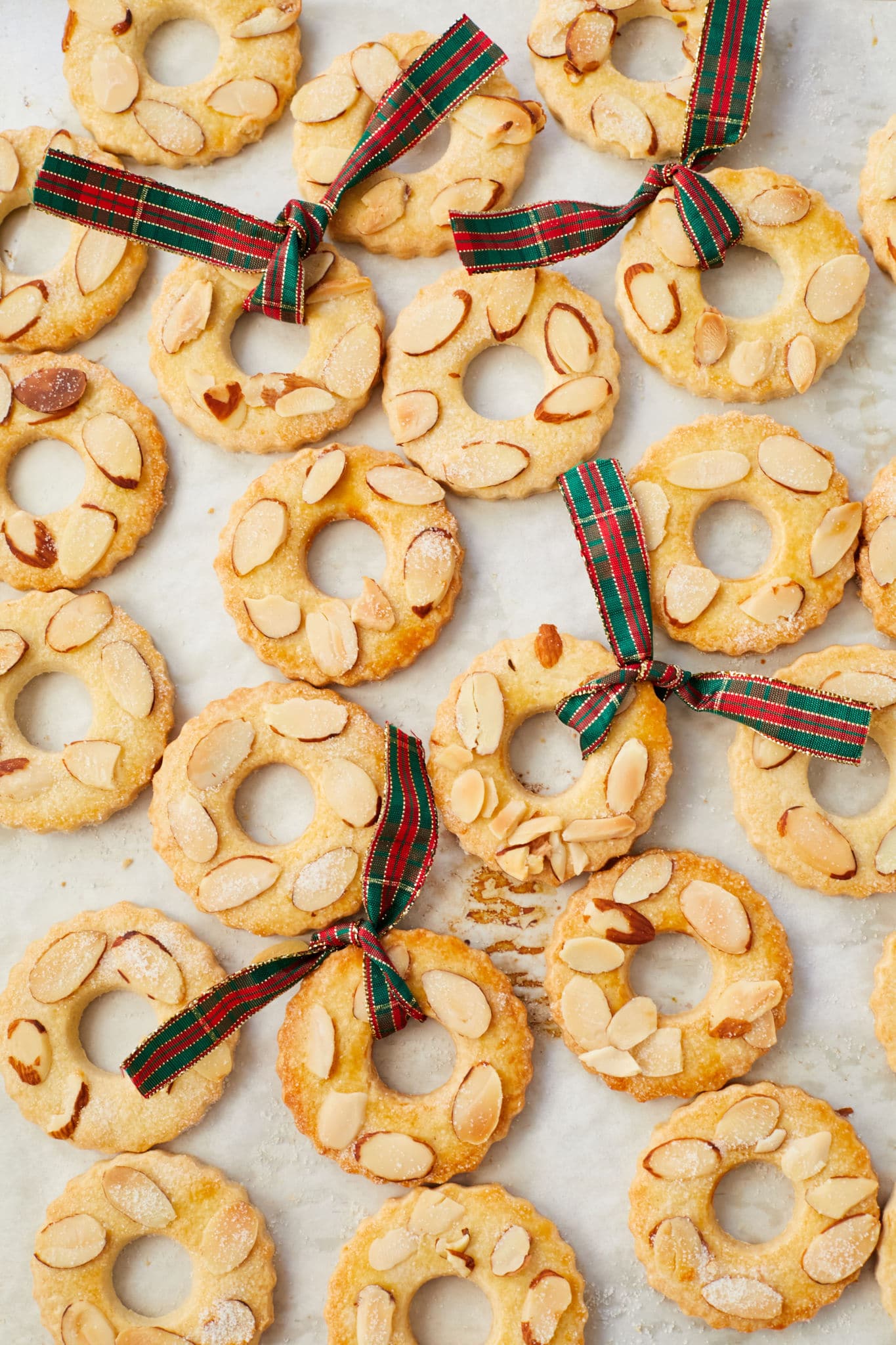 Homemade Dutch Kerstkransjes cookies on parchment paper. The traditional Dutch cookies are decorated with sliced almonds and some have a bow tied around them like a wreath. 
