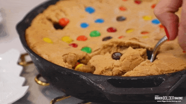 A scoop of cookie being pulled out of a skillet cookie.