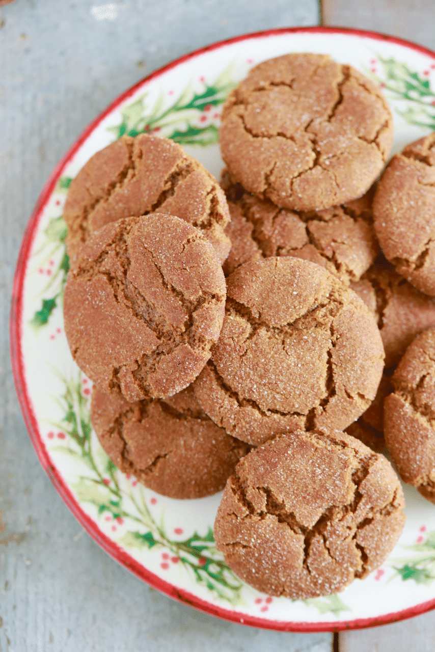 Soft, chewy molasses cookies are piled on top of a holiday plate that's decorated with holy berries.