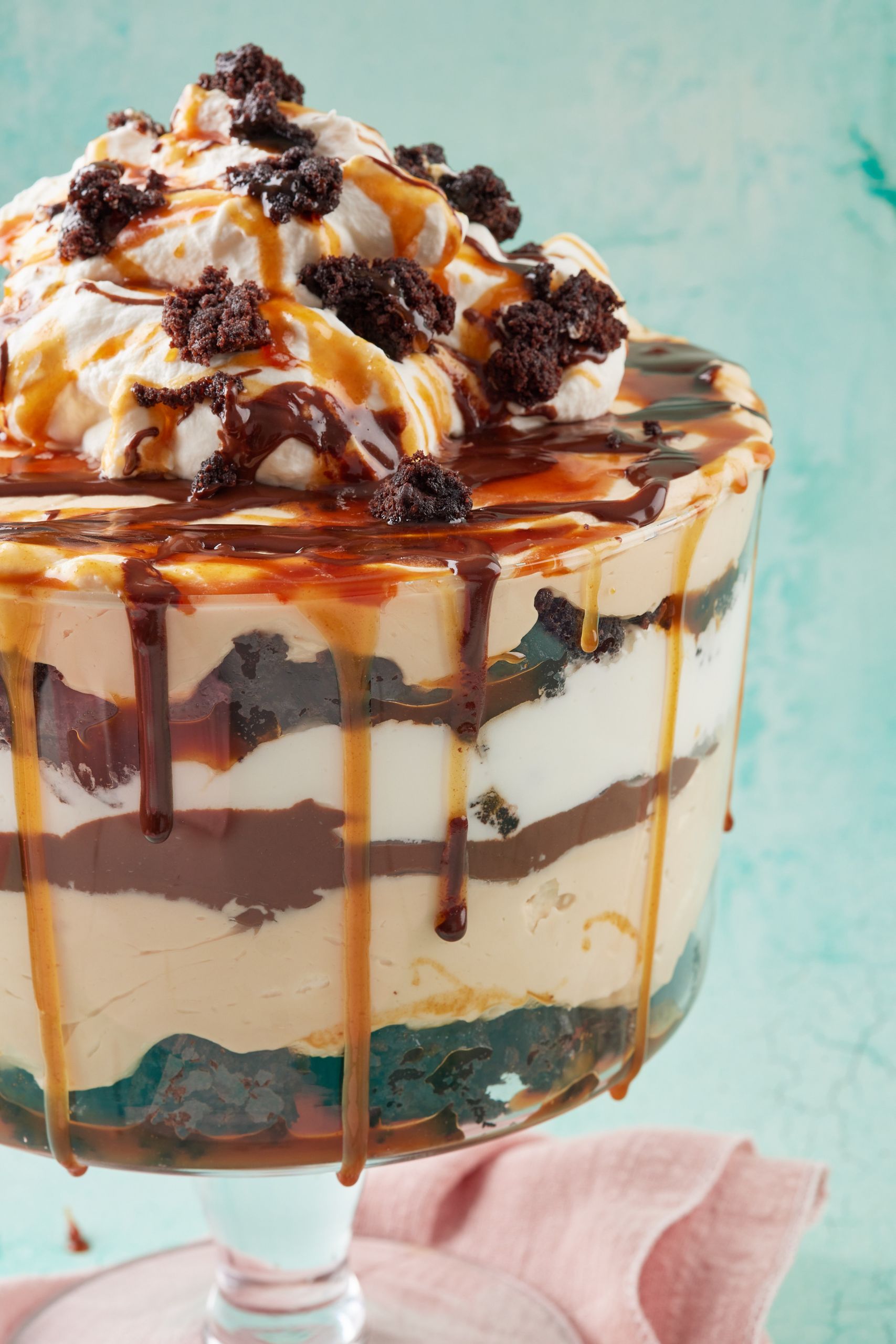 A big glass serving bowl of Chocolate Brownie Trifle with salted caramel dripping down the edge. It's topped with brownie bites. 