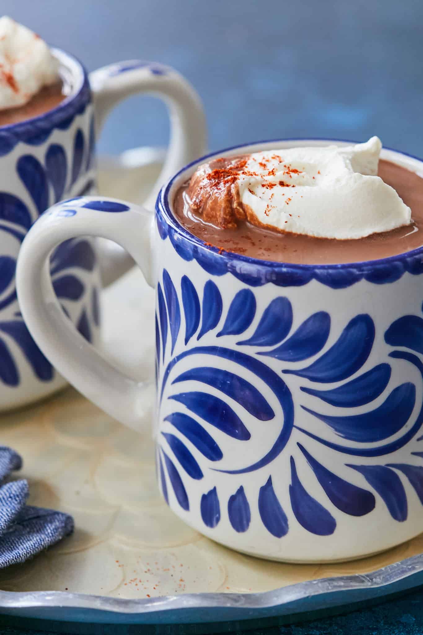 A blue mug of Mexican hot chocolate with whipped cream on top.