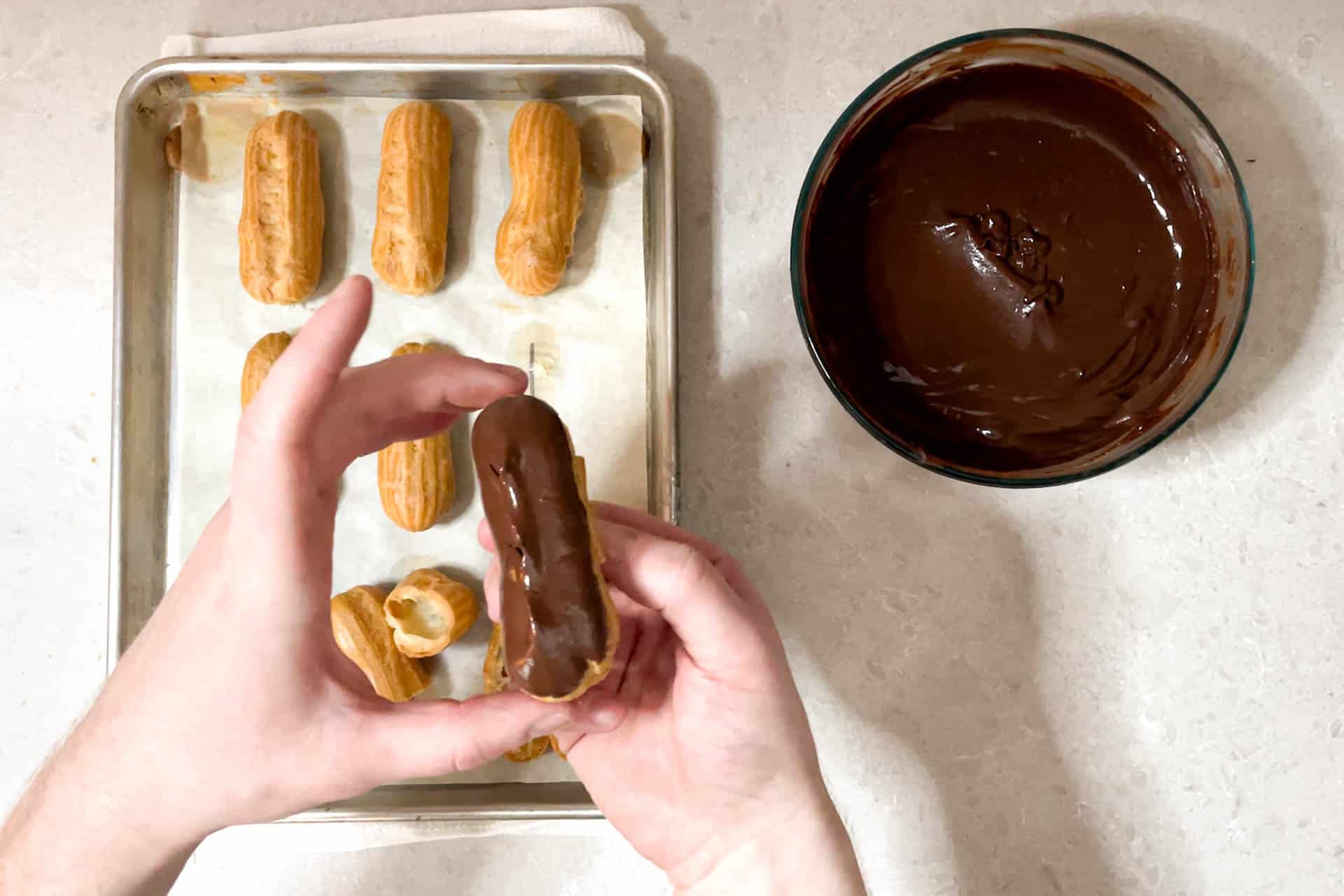 Eclairs being dipped in chocolate ganache.