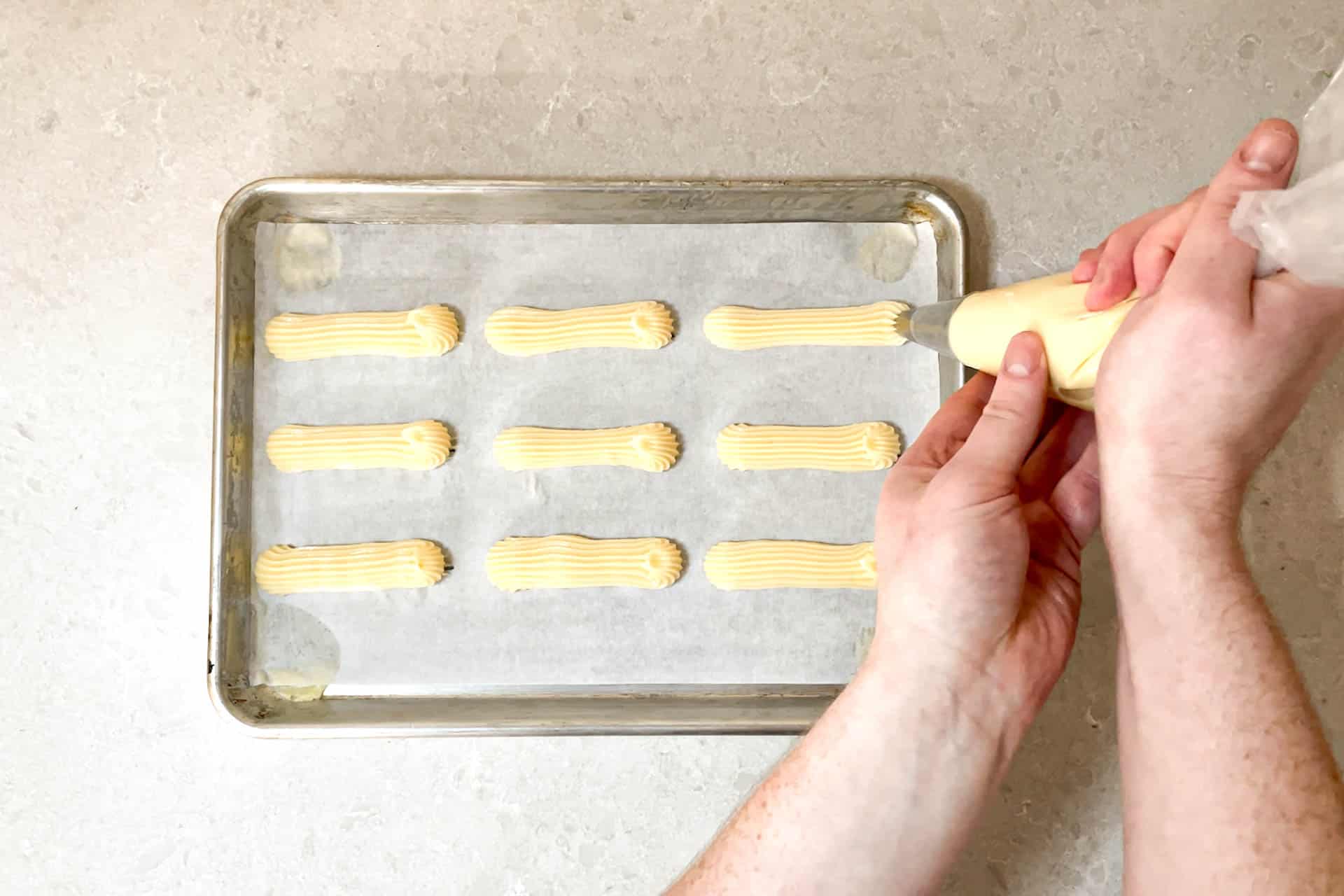 Piping the pâte à choux onto a baking sheet.