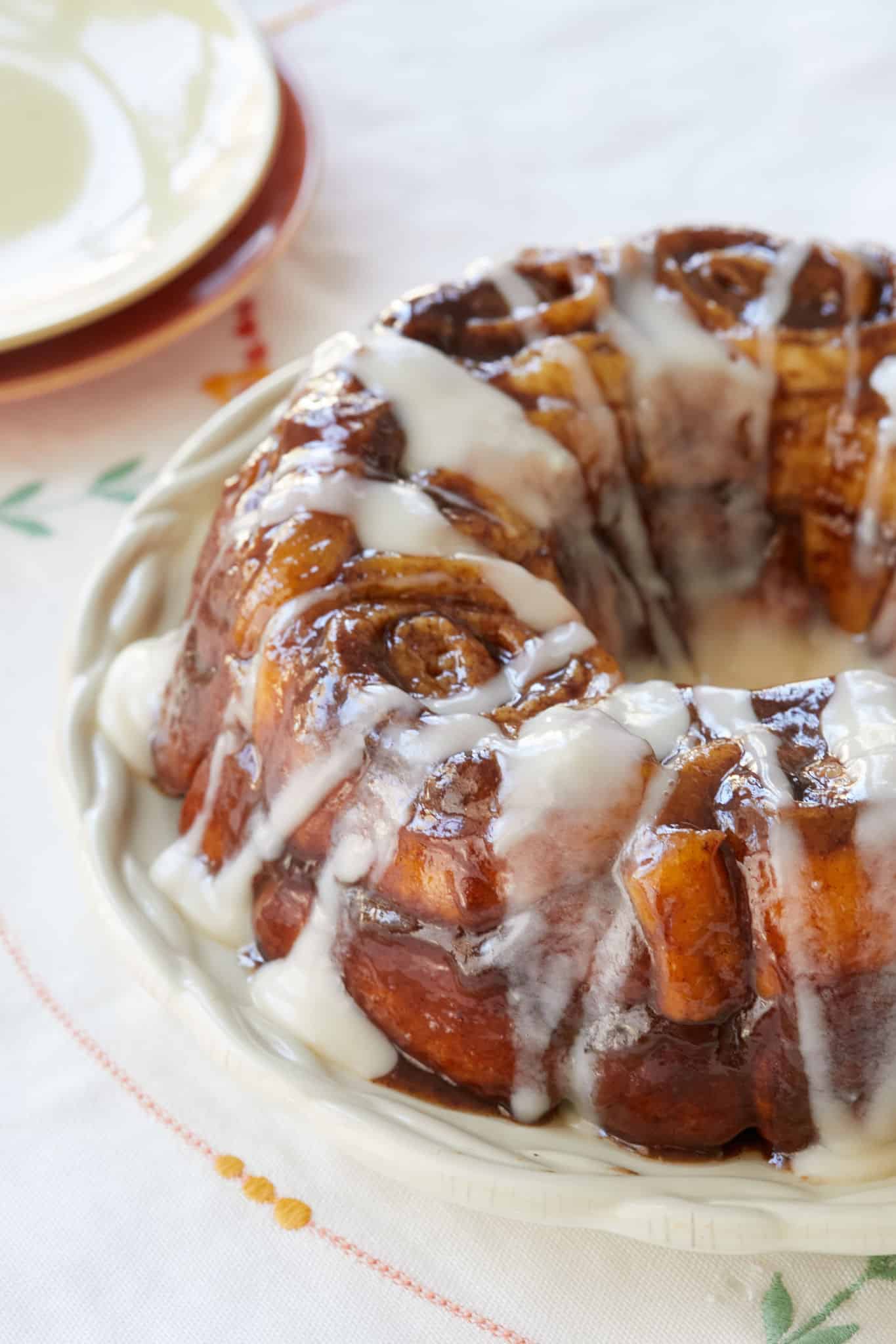 Heavenly Cinnamon Roll Monkey Bread is served on a white platter. The bread is soft, moist, packed with gooey cinnamon sugar filling and drizzled with a generous amount of cream cheese icing. 