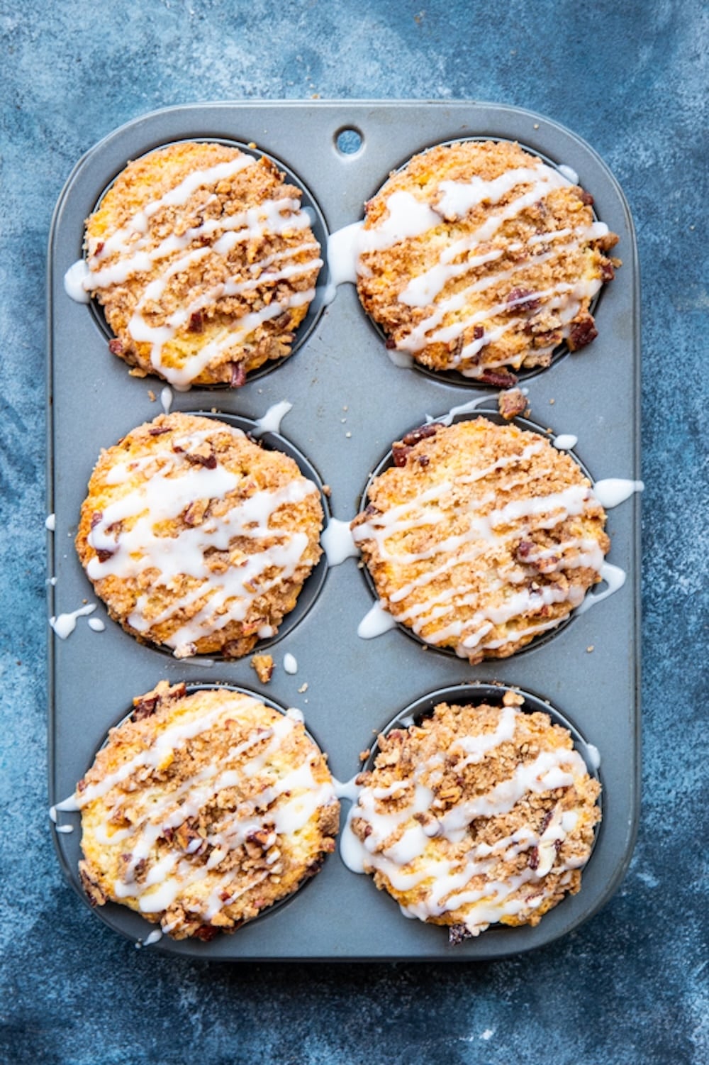  Top-down view of cinnamon roll muffins with glaze in the muffin tin. 