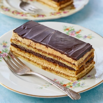 Two slices of This Classic Opera Cake are served, featuring layers of sponge cake, coffee syrup, French coffee buttercream, and chocolate butter glaze.