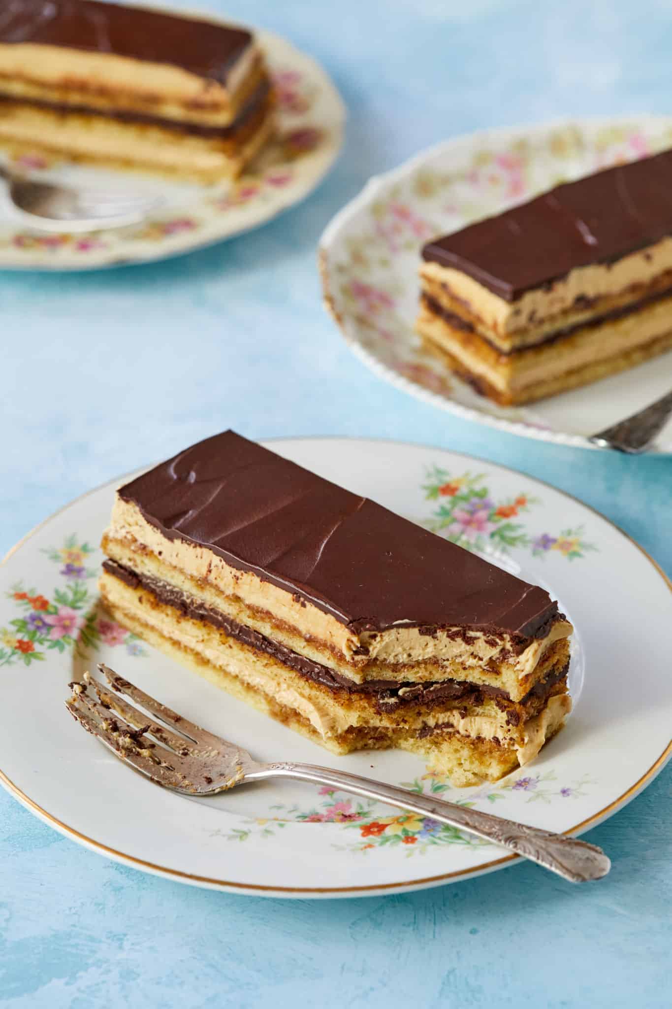 Three slices of This Classic Opera Cake are served, featuring layers of sponge cake, coffee syrup, French coffee buttercream, and chocolate butter glaze.