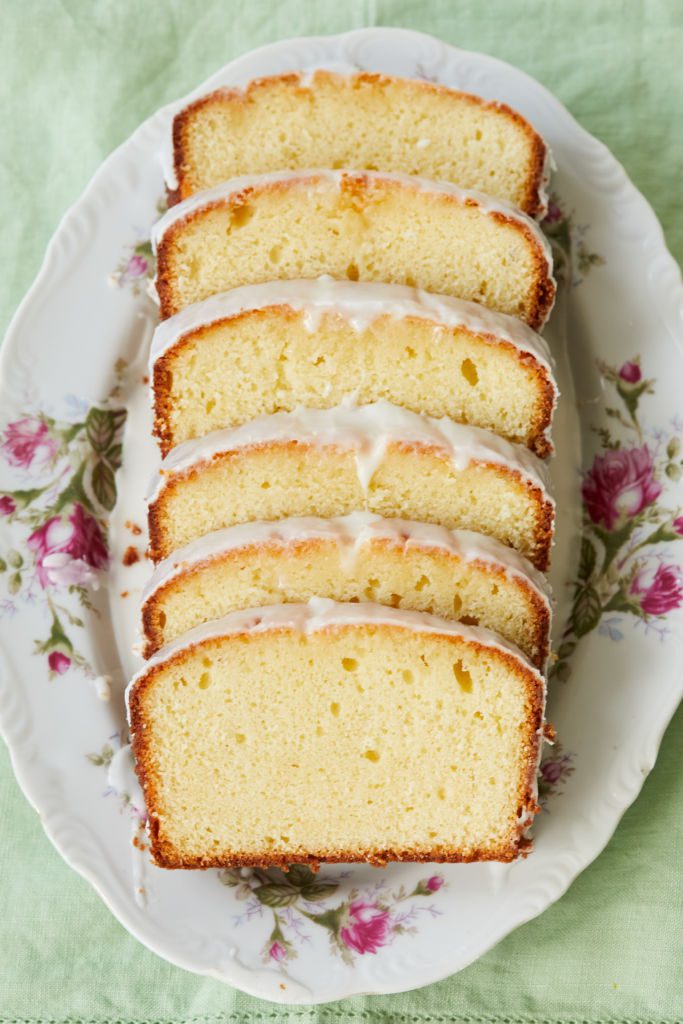 Soft, moist Lemon Yogurt Loaf Cake is sliced and frosted on a floral platter.