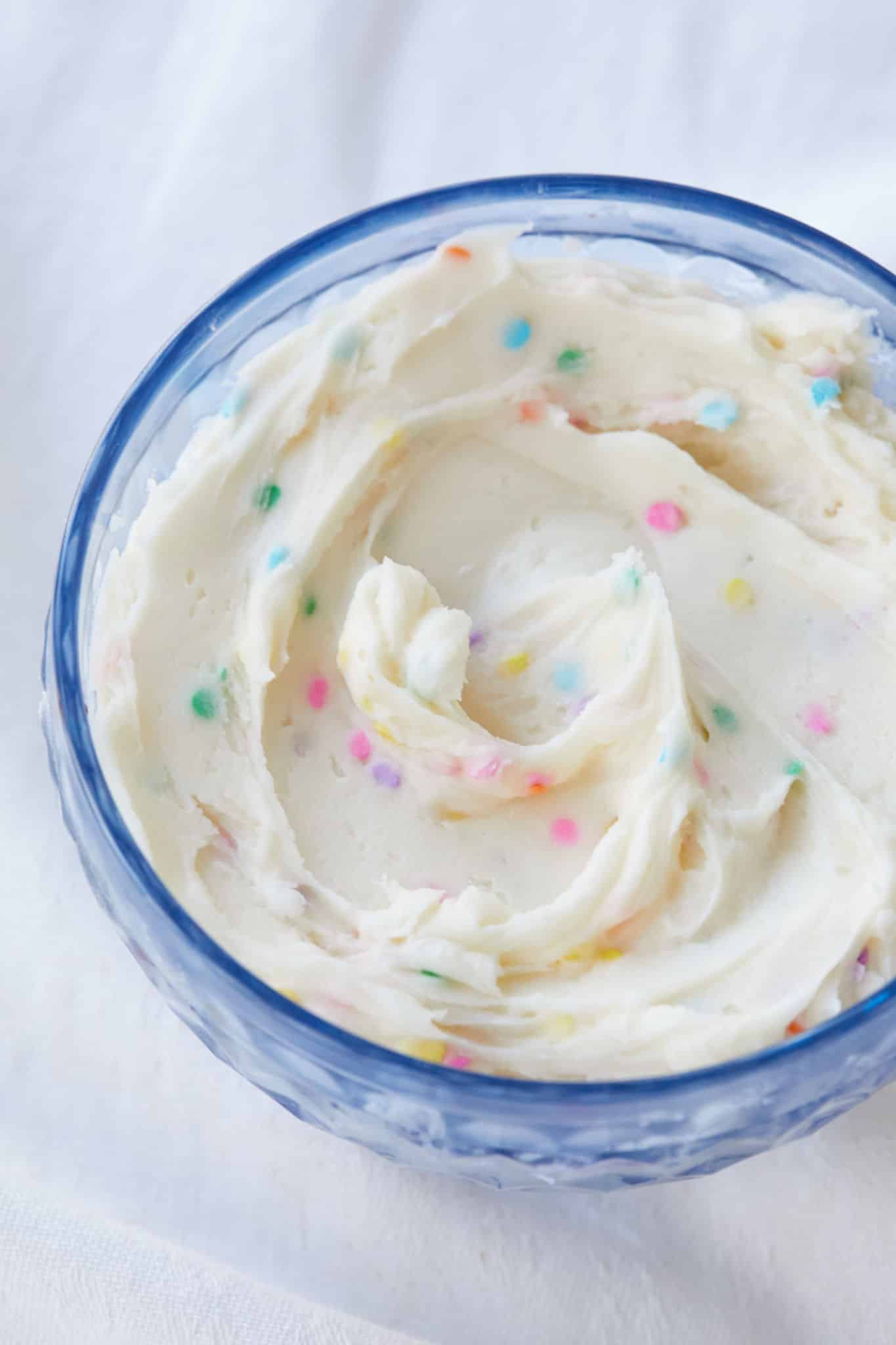 A top-down view of funfetti frosting in a blue bowl.