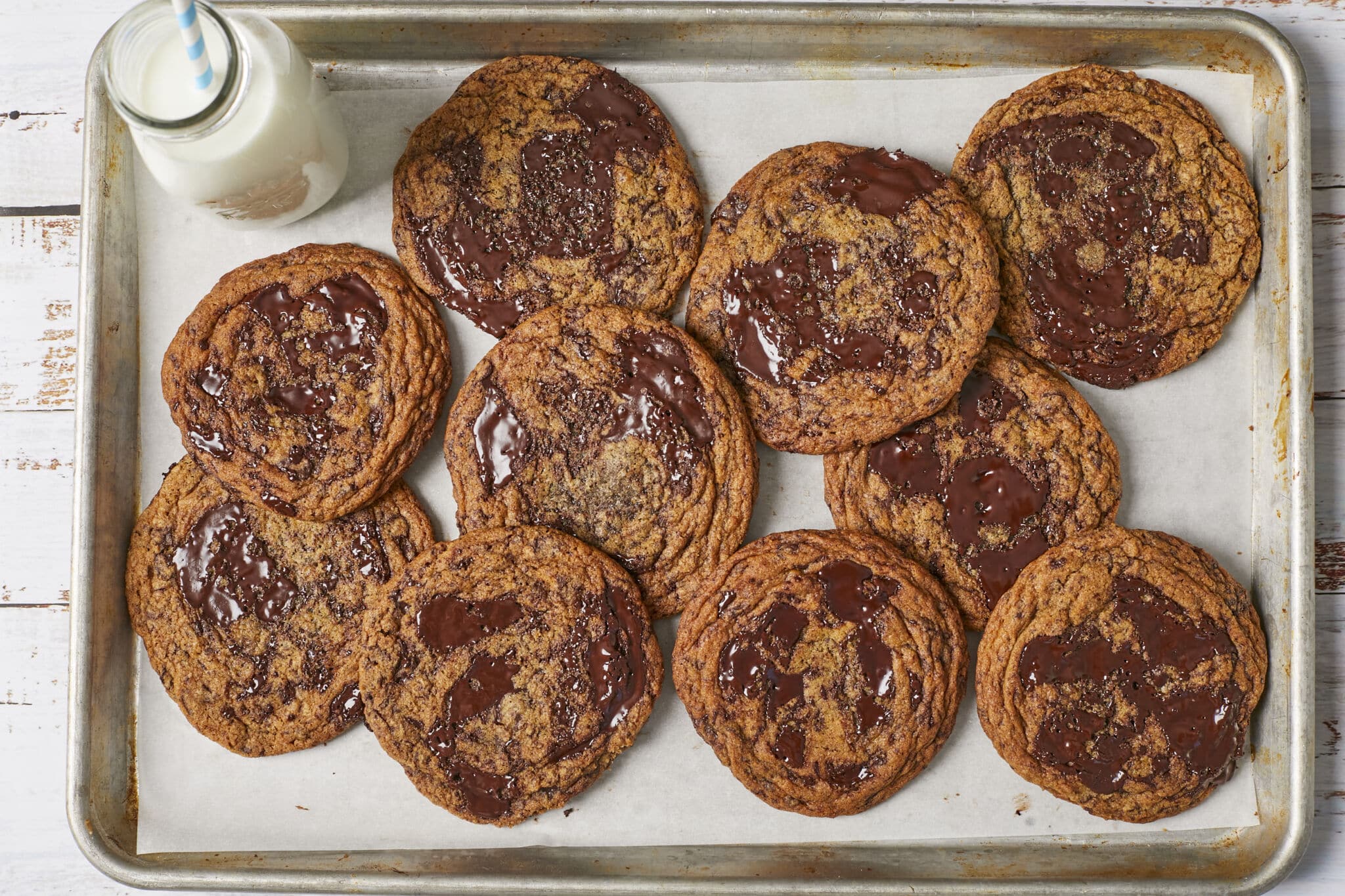 Best Ever Chocolate Chip Cookies on a baking tray, covered with crinkles on the surface and loaded with pools of melted chocolate in the center, to go perfectly with a glass of milk in the up left corner of the tray.