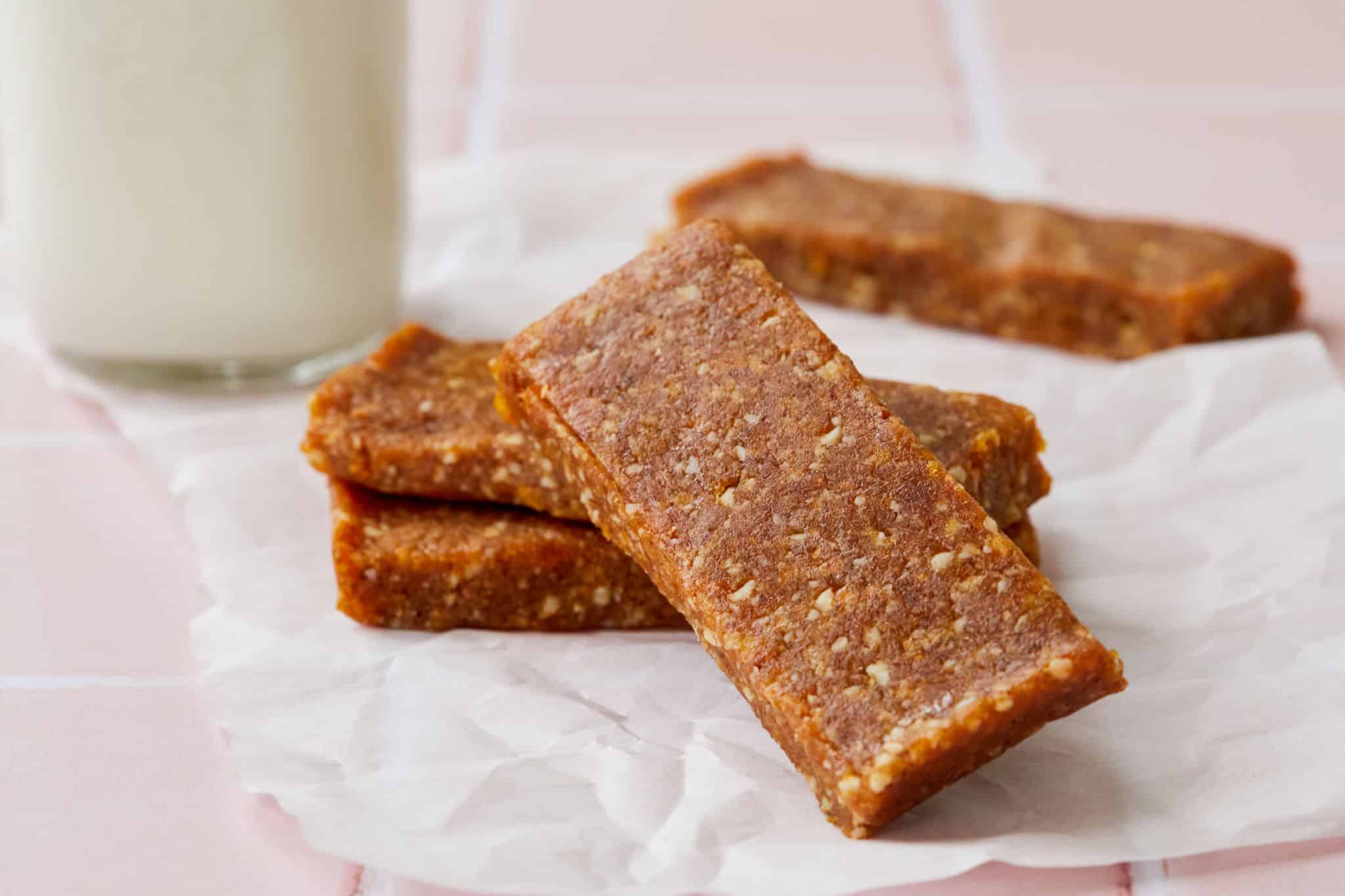 Four homemade Larabars made with three ingredients sit on a table next to a glass of milk.