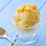 Ice cream made with coconut milk, mangos, and bananas is served in a glass serving cup, topped with fresh mangoes.