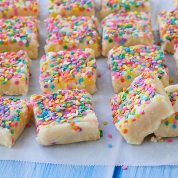 Homemade Birthday Cake Fudge is cut into squares and presented on parchment paper. The Funfetti Fudge is covered in rainbow sprinkles.