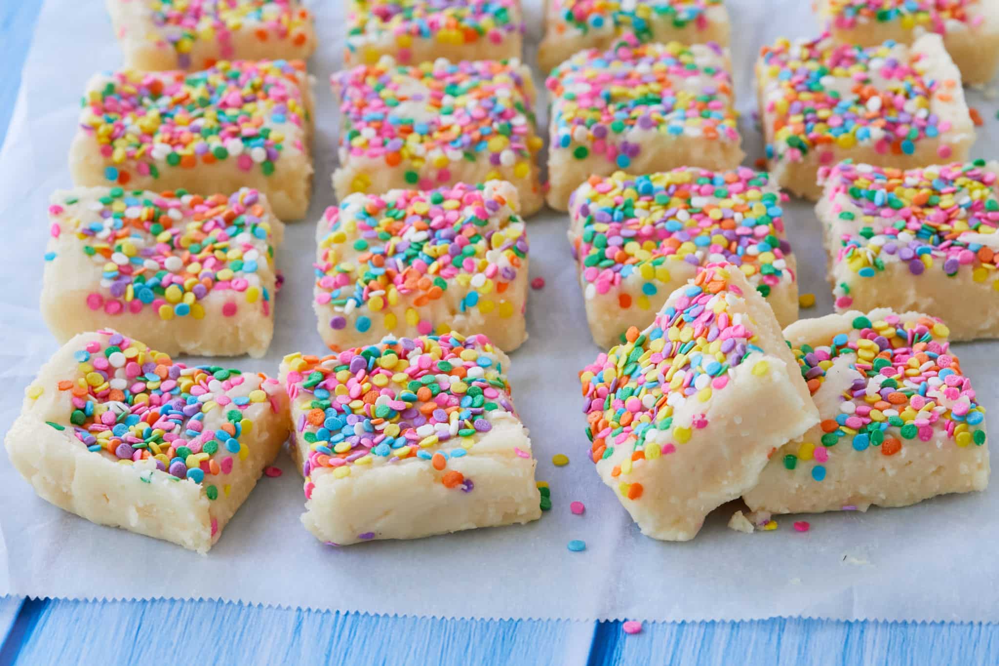 Homemade Birthday Cake Fudge is cut into squares and presented on parchment paper. The Funfetti Fudge is covered in rainbow sprinkles.