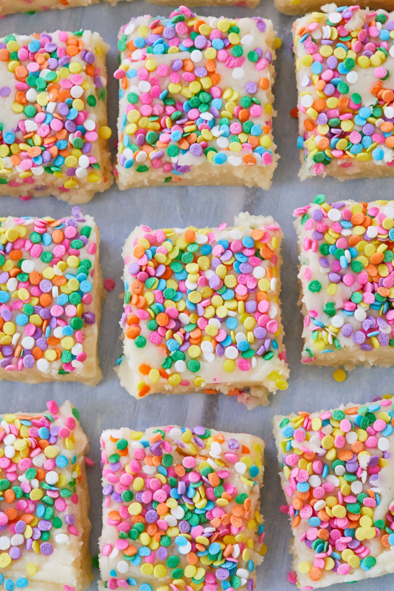 Homemade Funfetti Fudge is cut into squares. The white fudge is covered in rainbow sprinkles.