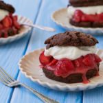 Three strawberry chocolate shortcakes are stuffed with fresh whipped cream and juicy strawberries on white plates.