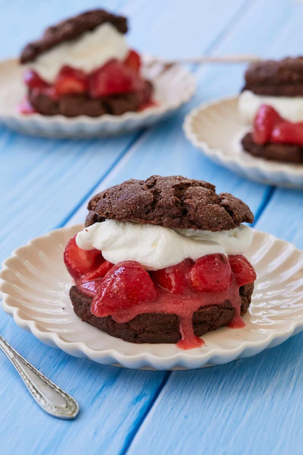 Three strawberry chocolate shortcakes are stuffed with fresh whipped cream and juicy strawberries on white plates.