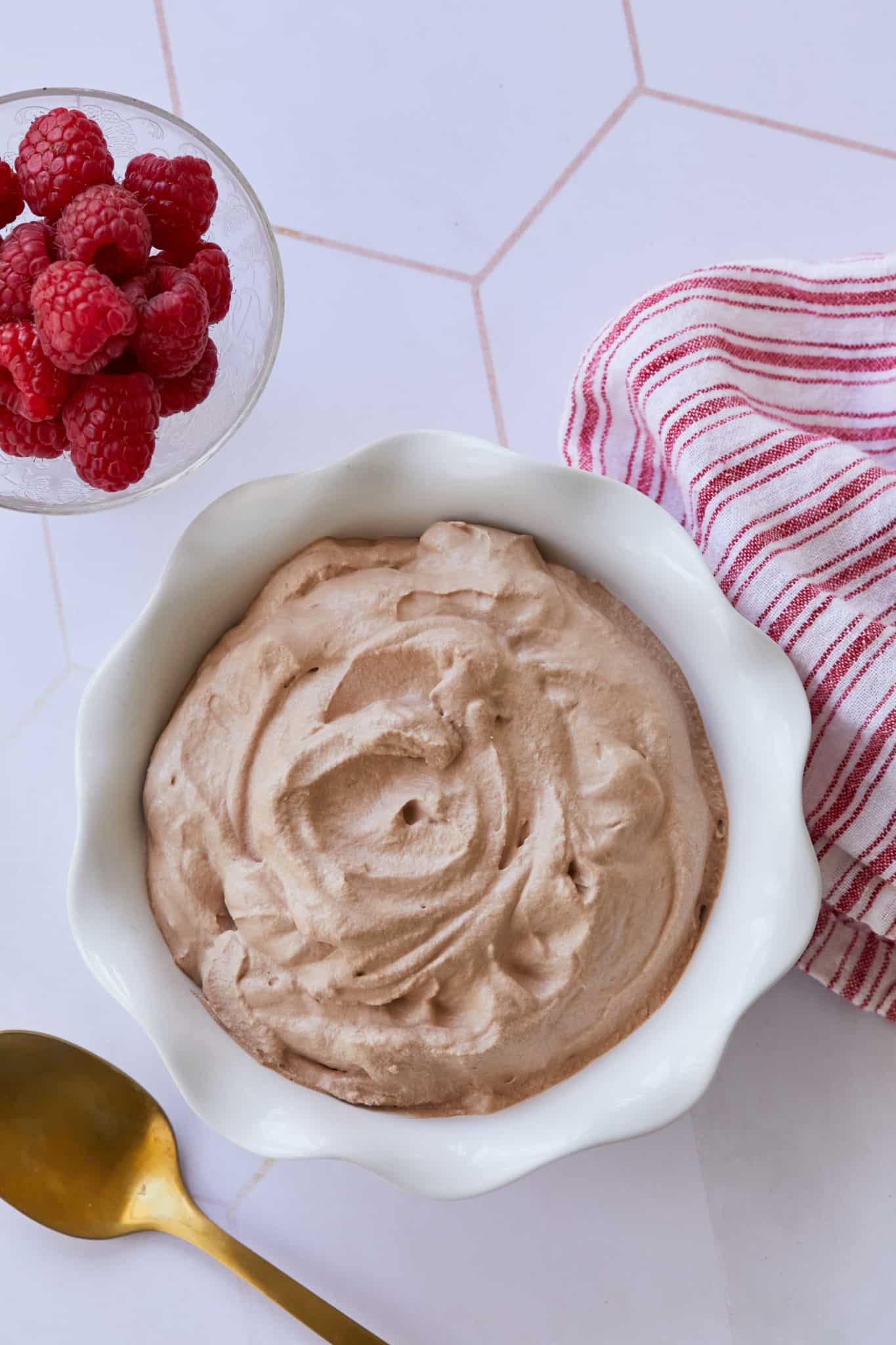 A while bowl filled with chocolate whipped cream sits besides a bowl of raspberries.