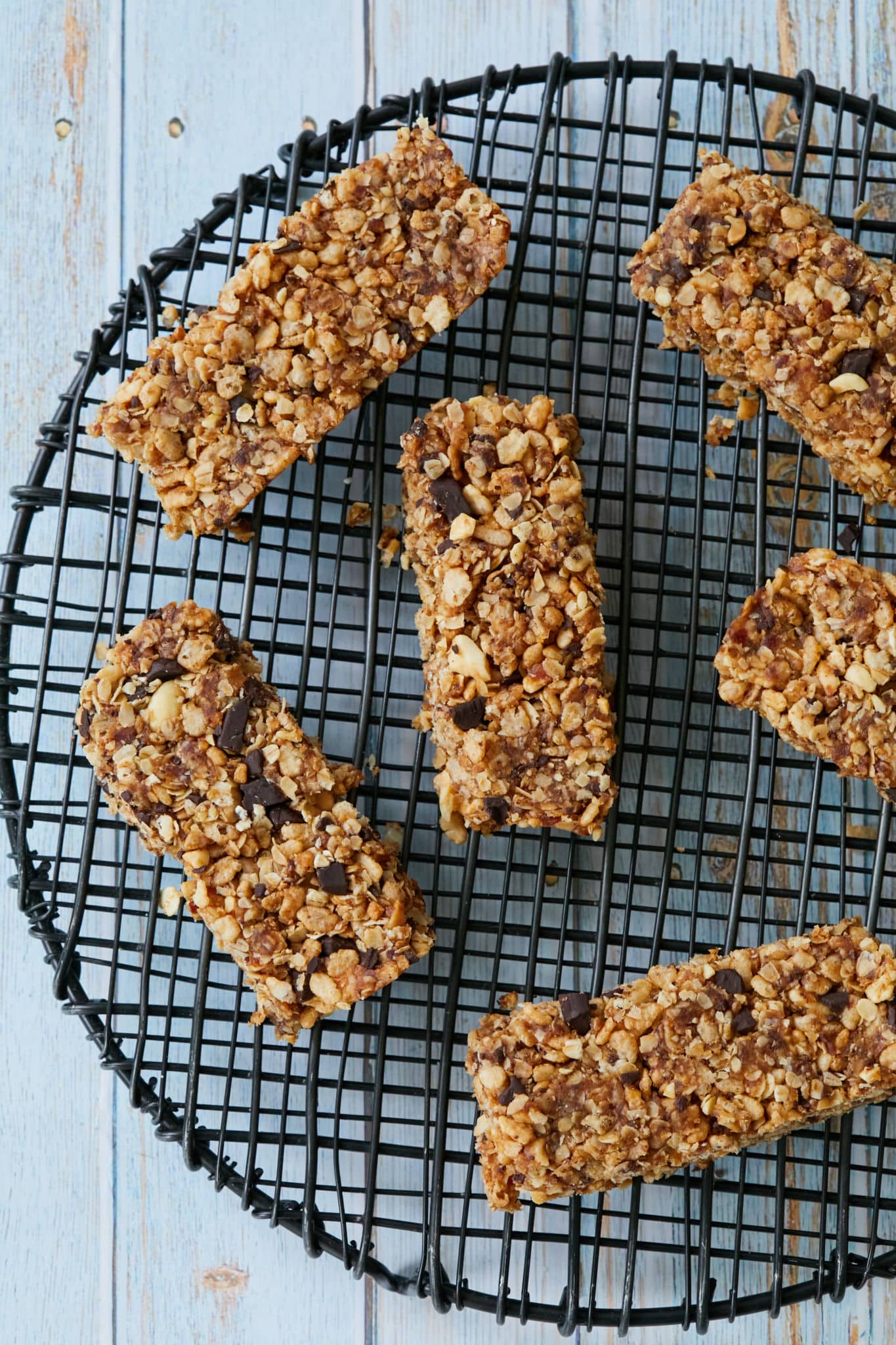 Homemade No Bake Clif Bars are displayed on a black wire rack over a blue table.