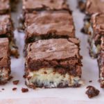 A batch of coconut macaroon brownies are displayed on a table, with chewy macaroon in the middle of two layers of fudgy brownies.