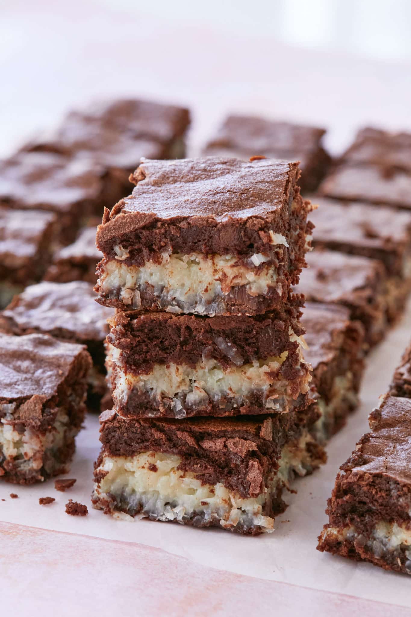 Three brownies with coconut macaroon filling are stacked up together next to other slices of the brownie recipe batch. The brownies are stuffed with coconut macaroon.
