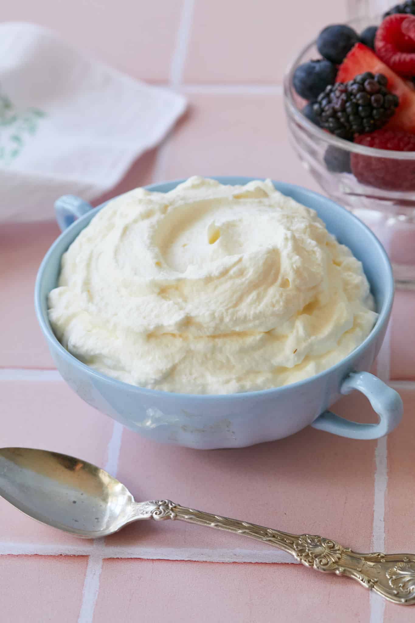 A bowl of Crème Fraiche Whipped Cream next to some fresh berries and a spoon